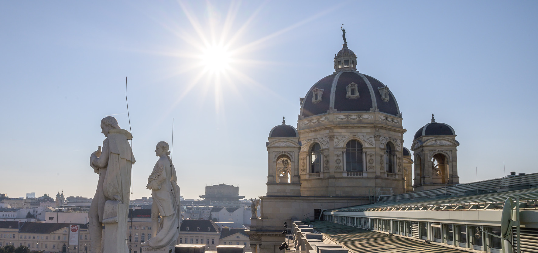 Dachfuehrung_©NHM Wien_Christina Rittmannsperger Blick auf die Kuppel des NHM Wien bei sonnigem Himmel mit zwei steinernen Figuren im Vordergrund