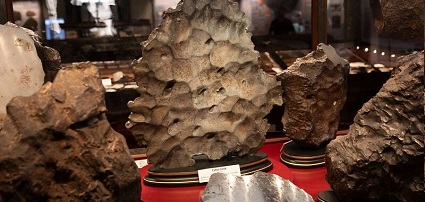 Mehrere unterschiedlich geformte Meteoriten auf roten Podesten in einer Vitrine eines Museums.