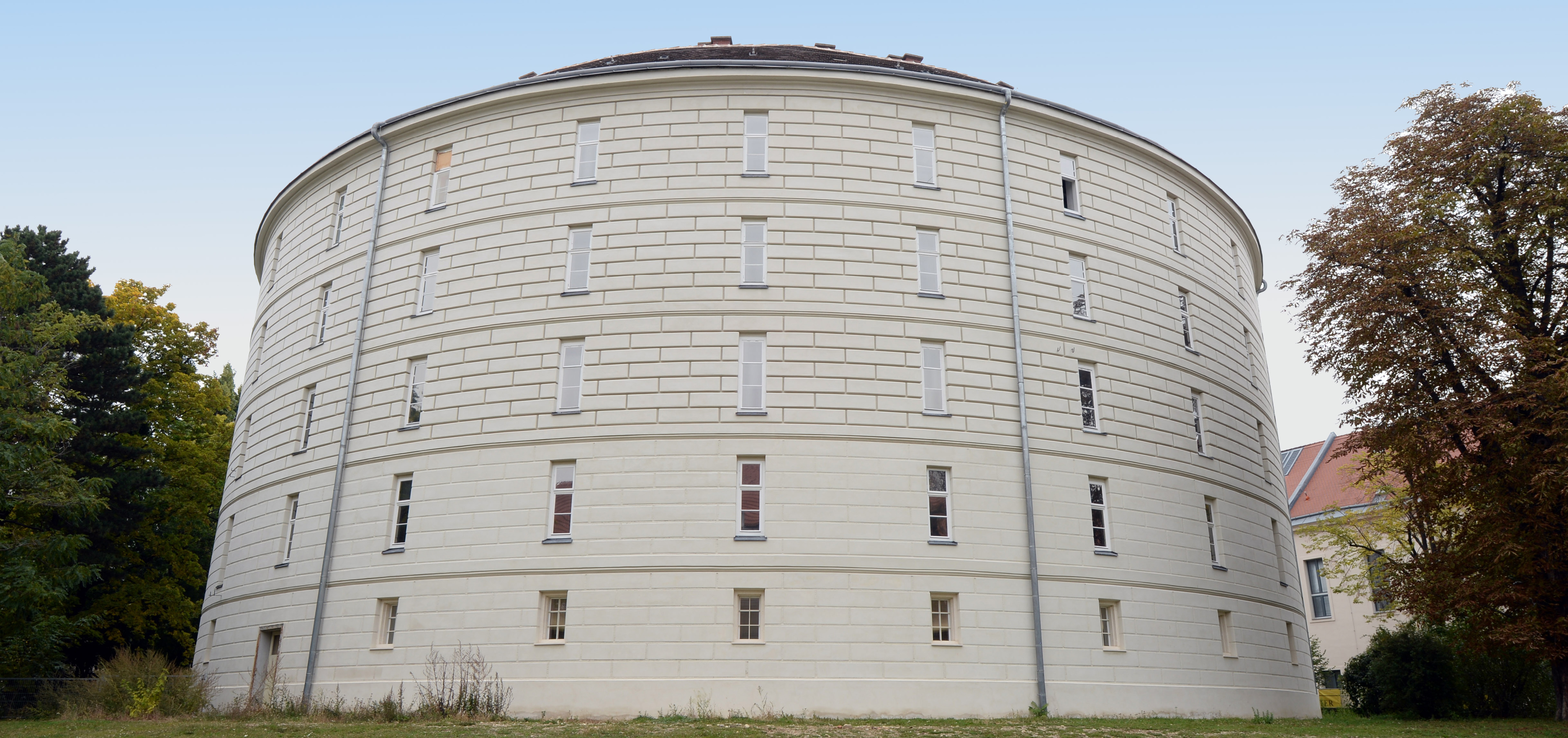 Narrenturm @Alice Schumacher, NHM Runder, weißer Narrenturm mit kleinen Fenstern, umgeben von Gras und Bäumen in Wien